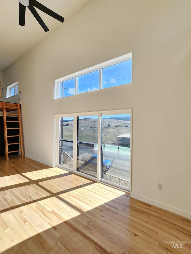 unfurnished living room with ceiling fan, a high ceiling, baseboards, stairs, and hardwood / wood-style floors