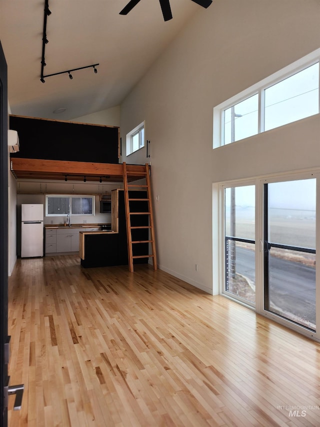 unfurnished living room featuring light wood-type flooring, a towering ceiling, a ceiling fan, and a sink