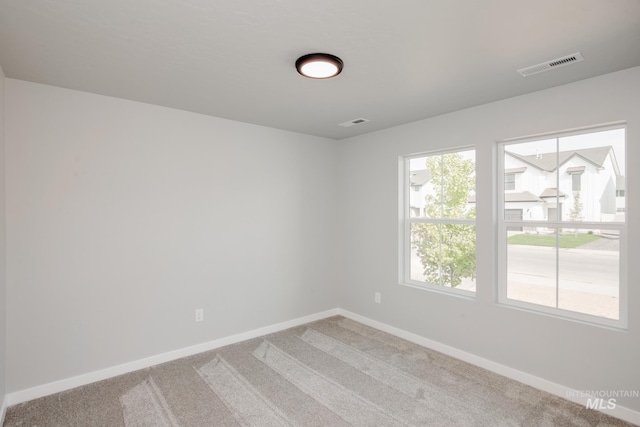empty room with carpet, baseboards, plenty of natural light, and visible vents
