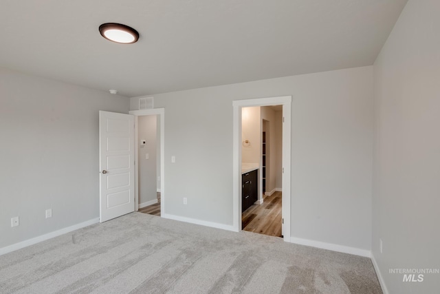 unfurnished bedroom featuring baseboards, ensuite bathroom, visible vents, and carpet floors