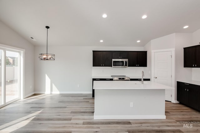 kitchen featuring stainless steel appliances, recessed lighting, light wood-style floors, a center island with sink, and light countertops