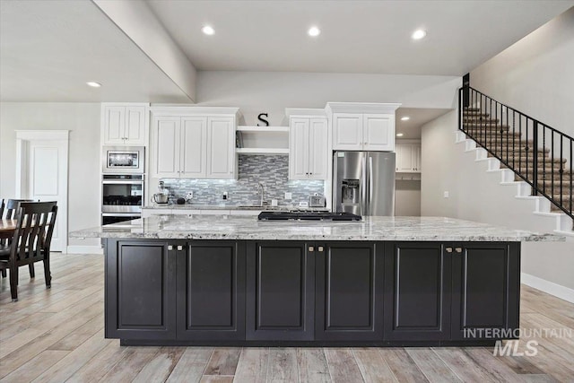 kitchen featuring appliances with stainless steel finishes, a spacious island, sink, light hardwood / wood-style floors, and white cabinetry