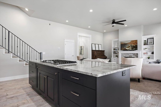 kitchen featuring ceiling fan, stainless steel gas cooktop, light hardwood / wood-style floors, a fireplace, and a kitchen island