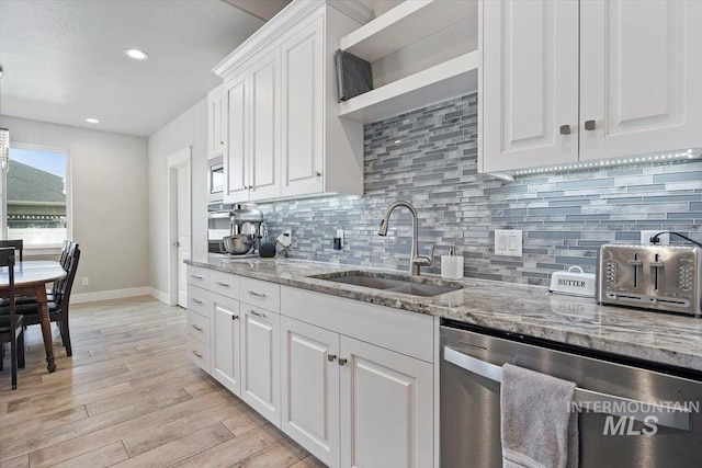 kitchen with tasteful backsplash, light stone counters, stainless steel dishwasher, sink, and white cabinets