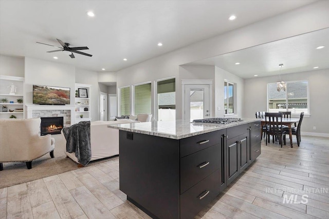 kitchen with pendant lighting, a stone fireplace, built in shelves, a kitchen island, and stainless steel gas cooktop