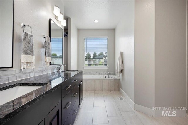 bathroom with tile patterned floors, vanity, a relaxing tiled tub, and a textured ceiling