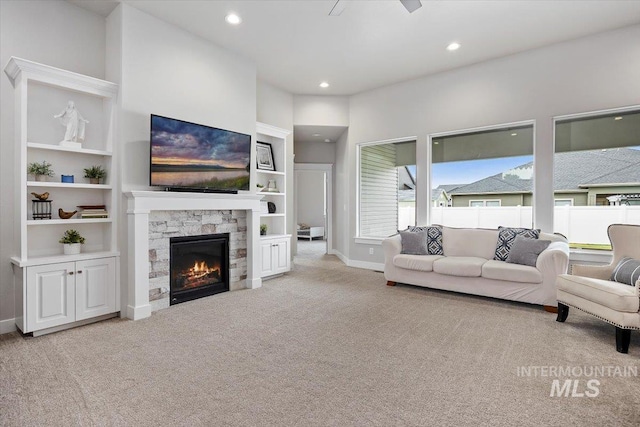 living room featuring built in shelves, light colored carpet, a stone fireplace, and ceiling fan