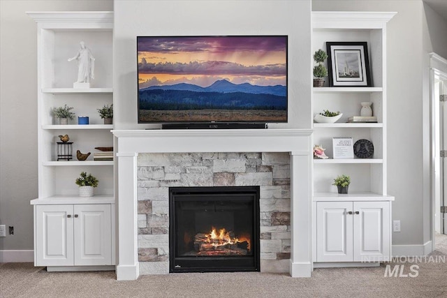 carpeted living room with built in shelves and a stone fireplace