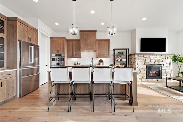 kitchen featuring a center island with sink, a breakfast bar, a stone fireplace, and appliances with stainless steel finishes