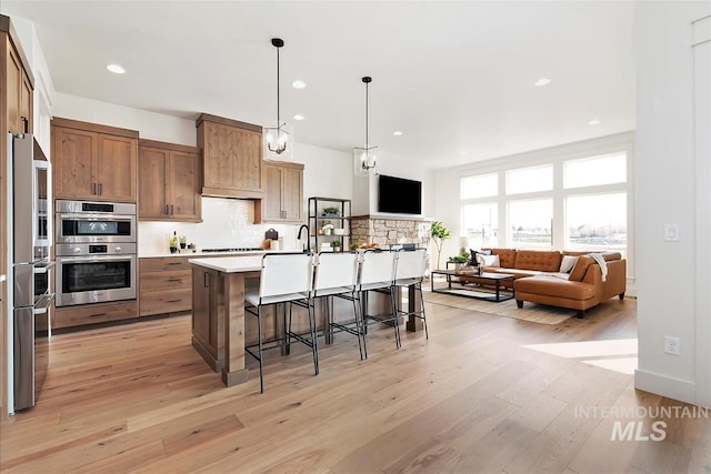 kitchen with stainless steel appliances, hanging light fixtures, a kitchen breakfast bar, a kitchen island with sink, and light wood-type flooring