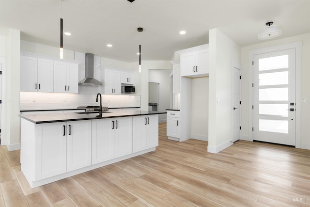 kitchen featuring white cabinets, a center island with sink, and wall chimney range hood