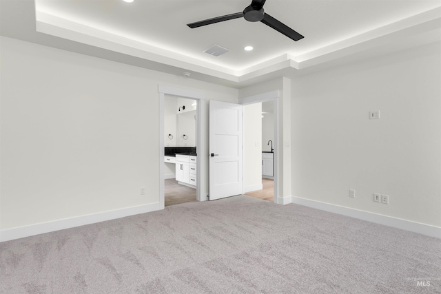 unfurnished bedroom with ensuite bathroom, ceiling fan, a tray ceiling, and light colored carpet