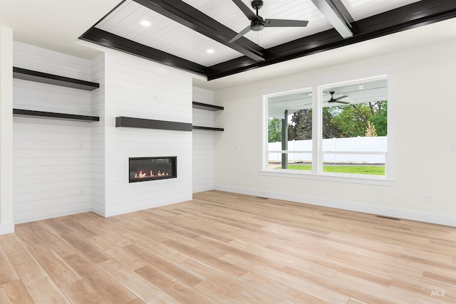 unfurnished living room featuring ceiling fan, a large fireplace, light hardwood / wood-style floors, coffered ceiling, and beam ceiling