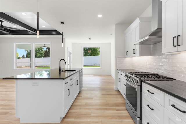 kitchen featuring wall chimney range hood, a kitchen island with sink, beam ceiling, appliances with stainless steel finishes, and sink