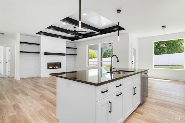 kitchen featuring a large fireplace, an island with sink, white cabinets, and pendant lighting