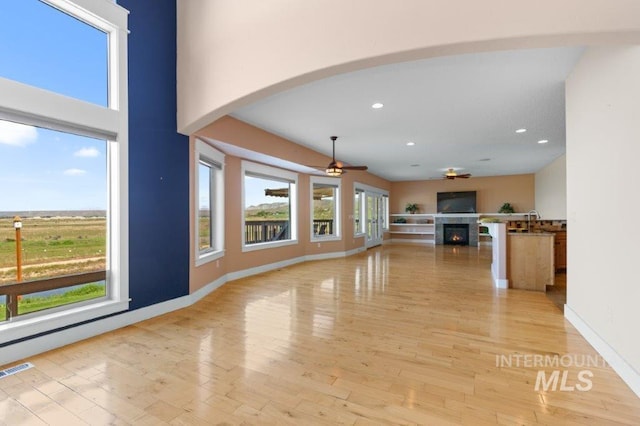2600 W S Slope Rd, Emmett, ID 83617 - unfurnished living room featuring a ceiling fan, a warm lit fireplace, recessed lighting, arched walkways, and light wood-style floors
