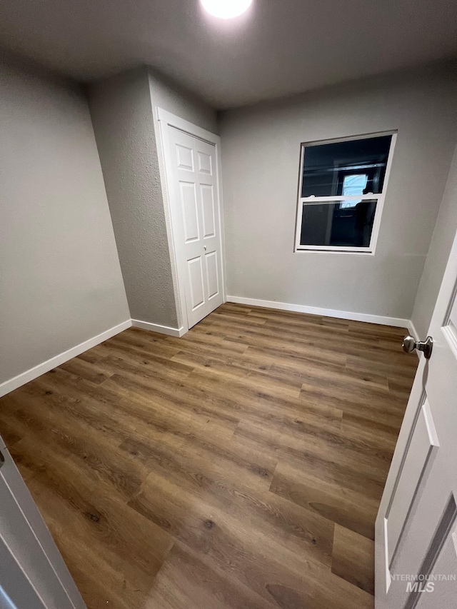 unfurnished bedroom featuring baseboards, wood finished floors, and a closet