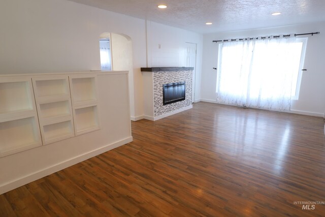 unfurnished living room with a fireplace, dark wood-type flooring, and a textured ceiling