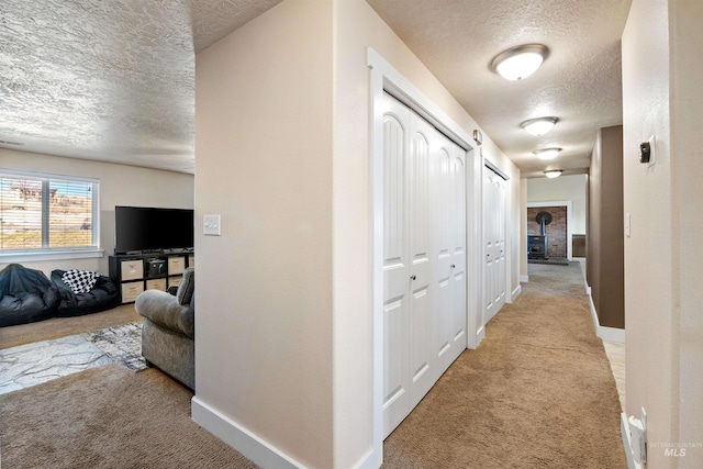 corridor with a textured ceiling, baseboards, and light carpet