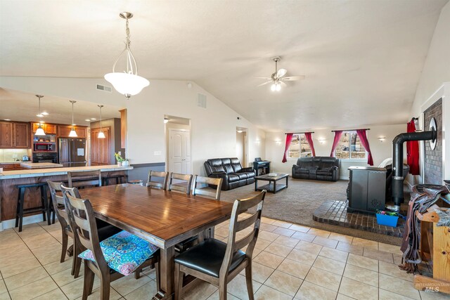 dining area featuring visible vents, lofted ceiling, light tile patterned floors, a wood stove, and a ceiling fan