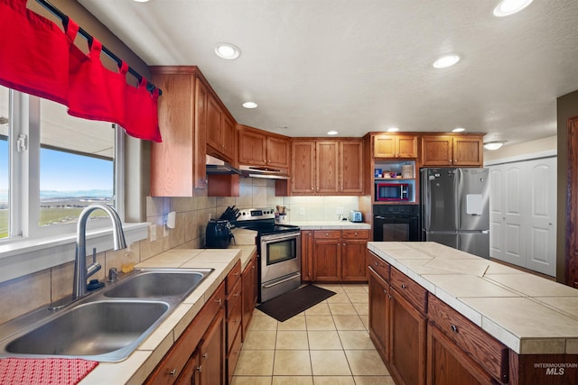 kitchen with light tile patterned floors, tile countertops, stainless steel appliances, and a sink