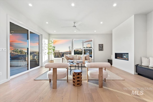 living room featuring ceiling fan, a large fireplace, and light wood-type flooring