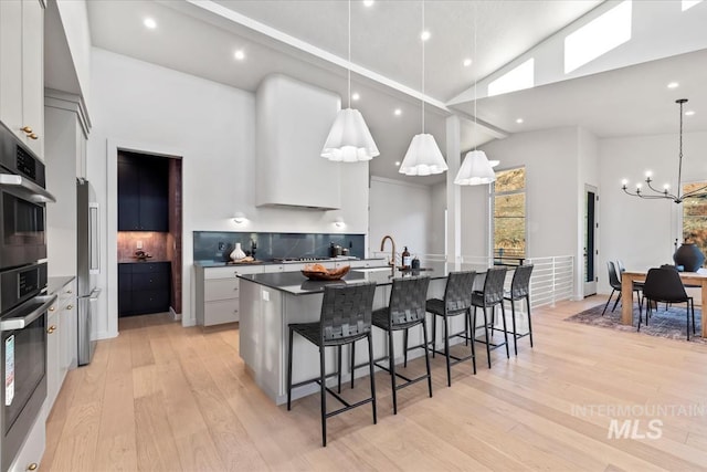 kitchen with white cabinetry, a large island, appliances with stainless steel finishes, hanging light fixtures, and high vaulted ceiling