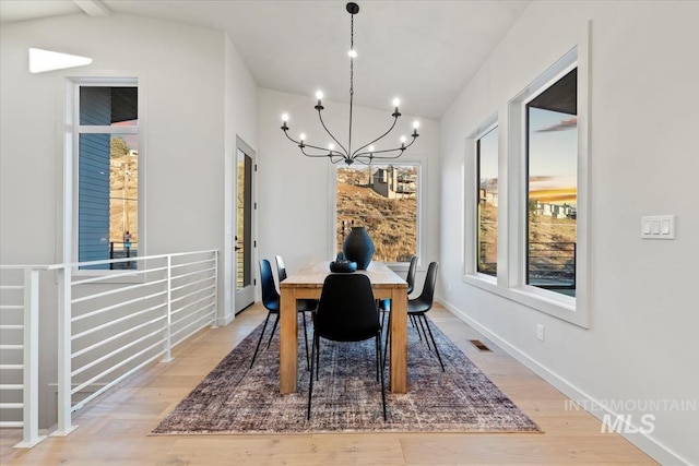 dining area featuring vaulted ceiling, an inviting chandelier, and light hardwood / wood-style floors