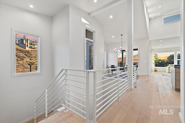 corridor featuring a wealth of natural light, light hardwood / wood-style flooring, lofted ceiling with beams, and a notable chandelier