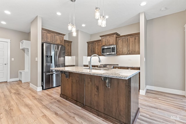 1073 W Smoky Quartz St, Kuna, ID 83634 - kitchen featuring stainless steel appliances, light stone counters, a breakfast bar area, a sink, and baseboards