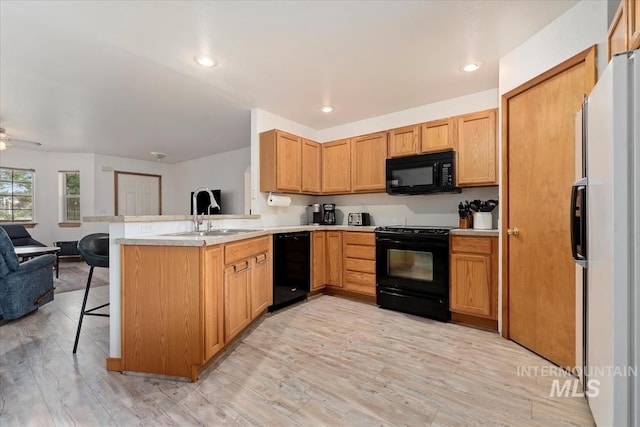 kitchen with a peninsula, open floor plan, light countertops, a sink, and black appliances