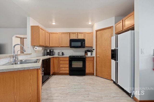 kitchen featuring a sink, light countertops, a peninsula, light wood-type flooring, and black appliances