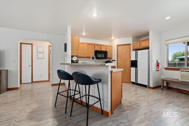 kitchen with a kitchen breakfast bar, black microwave, white refrigerator with ice dispenser, light wood-type flooring, and a peninsula
