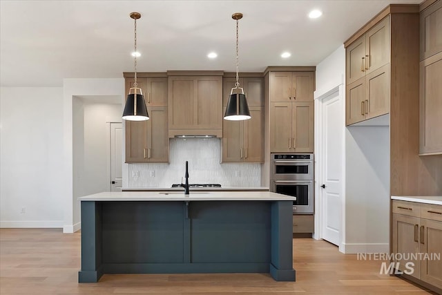 kitchen with light countertops, appliances with stainless steel finishes, light wood-type flooring, decorative backsplash, and a center island with sink