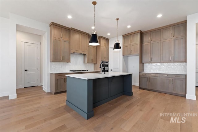 kitchen featuring light wood-type flooring, cooktop, light countertops, and a sink