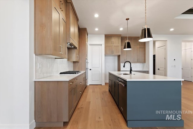 kitchen featuring a kitchen island with sink, light wood-style flooring, a sink, light countertops, and backsplash