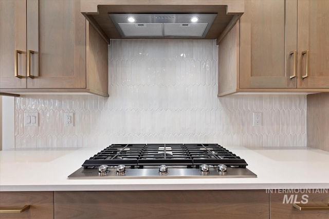 kitchen with custom range hood, stainless steel gas stovetop, light countertops, and backsplash