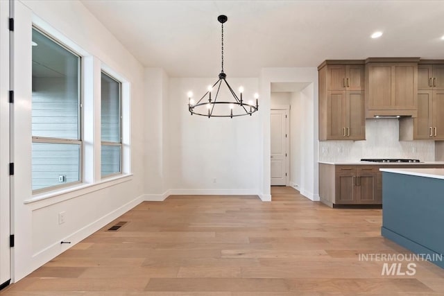 kitchen featuring tasteful backsplash, baseboards, light wood-style flooring, gas stovetop, and pendant lighting