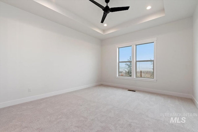 empty room featuring light carpet, a tray ceiling, recessed lighting, and baseboards