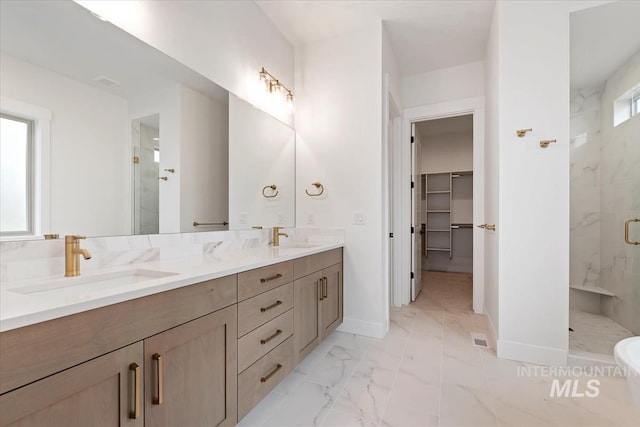 bathroom with marble finish floor, a spacious closet, a sink, and a stall shower