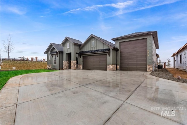 view of front of house with driveway, a garage, stone siding, central air condition unit, and board and batten siding