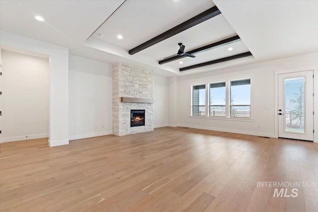 unfurnished living room featuring baseboards, a ceiling fan, a stone fireplace, light wood-type flooring, and beam ceiling