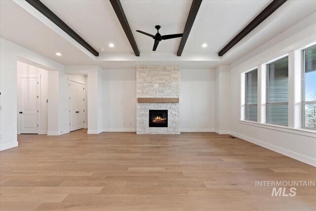 unfurnished living room with baseboards, a stone fireplace, beamed ceiling, and light wood-style floors