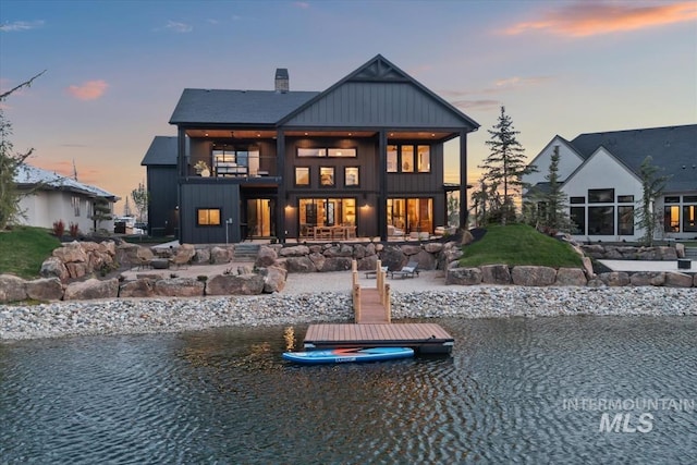 back of house at dusk featuring a patio area, a chimney, a balcony, and a water view