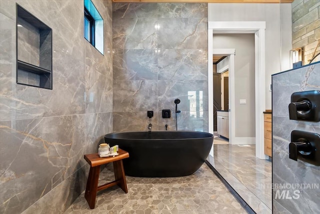 full bath featuring marble finish floor, baseboards, a soaking tub, and tile walls