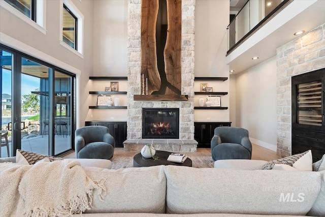 living area featuring baseboards, wood finished floors, a stone fireplace, and a high ceiling