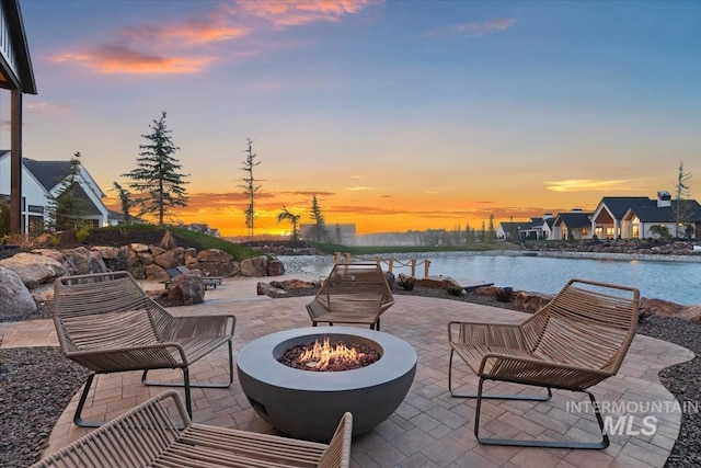 patio terrace at dusk featuring a water view and an outdoor fire pit