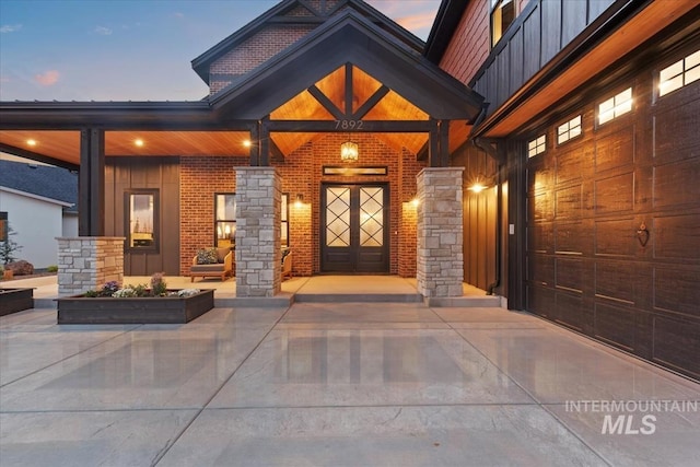 exterior entry at dusk with board and batten siding, stone siding, and covered porch