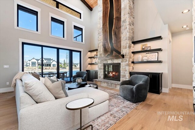 living area featuring high vaulted ceiling, a fireplace, baseboards, and light wood-style flooring
