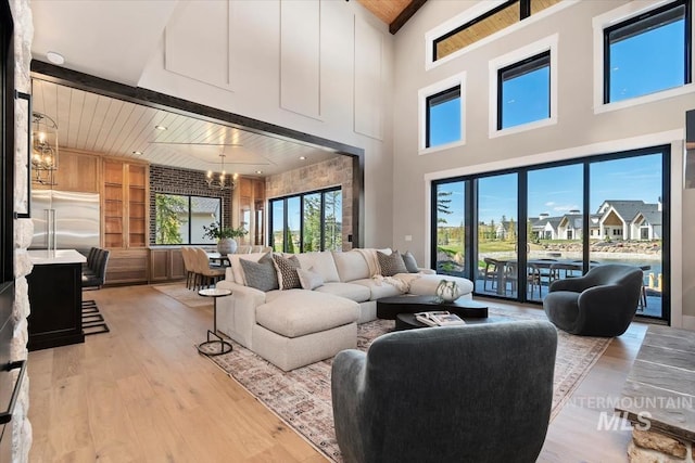 living room featuring light wood-style floors, a notable chandelier, built in shelves, a high ceiling, and wooden ceiling